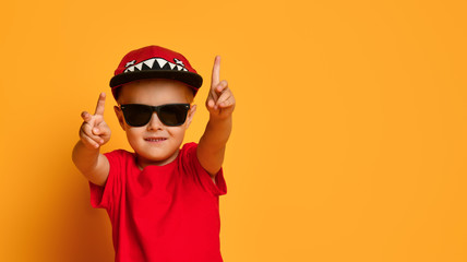 Young guy boy in a red T-shirt and dark pants, white sneakers and a funny cap posing on a free copy space on a yellow background