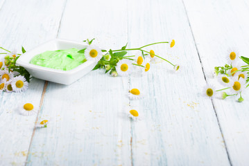 green cosmetis cream with chamomile flowers on white wooden table