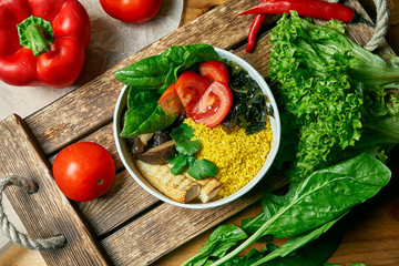 Vegetarian bowl with couscous tomatoes, spinach, tofu cheese and shiitaki mushrooms on a wooden tray in a composition with vegetables. Top view food flat lay