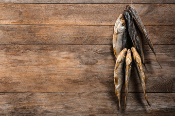 Dried fish hanging on rope against wooden background, space for text