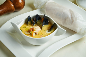 Close up view on fresh homemade Waterzooi soup - stew dish from Belgium. Yellow cream soup mussel and shrimp in white bowl. Restaurant food