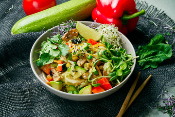 Vegetable vegan wok in a gray bowl on a gray cloth in a composition with vegetables. Delicious vegetarian food. Diet Menu. Close up