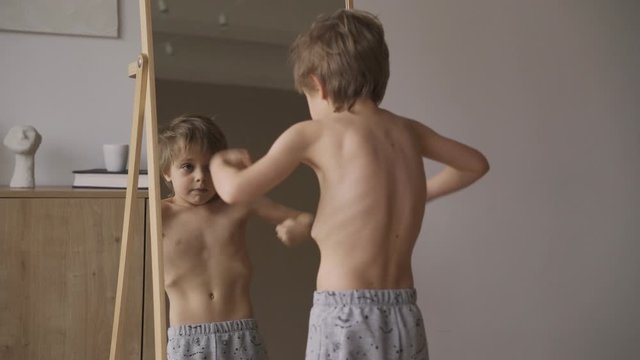 Cute caucasian boy showing muscles in front mirror, sport power, health care