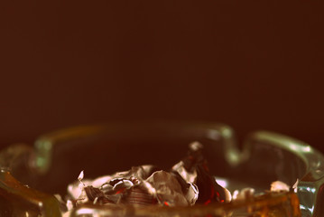 A crumpled sheet of paper burns in a glass ashtray. Retro style