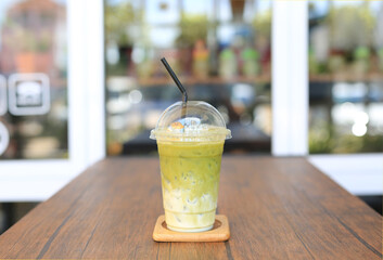 Iced matcha green tea latte with milk with brown straw in take away cup on wooden table at cafe.