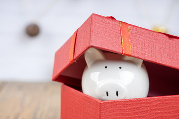 Piggy bang under red gift box on wooden background. Festive and financial concepts