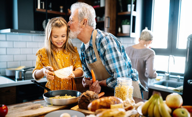 Happy young girl and her grandfather cooking together in kitchen