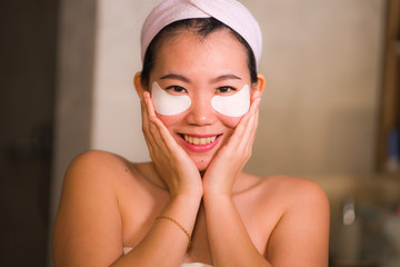 young beautiful and happy Asian Korean woman smiling to bathroom mirror applying hydrating eye...