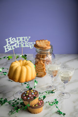 Fototapeta na wymiar Geburtstagsfeier mit Gugelhupf Kuchen, Muffins, Kekse Gebäck und Sekt mit Happy Birthday Dekoration und Kleeblättern zum Geburtstag
