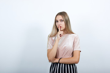 Obraz premium Portrait of cute smiling young woman in casual shirt putting hand prop up on mouth isolated on white wall background in studio. People sincere emotions, lifestyle concept.