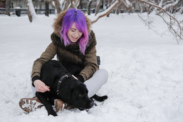 Fototapeta na wymiar A young woman plays with her pet black Labrador outside in winter.