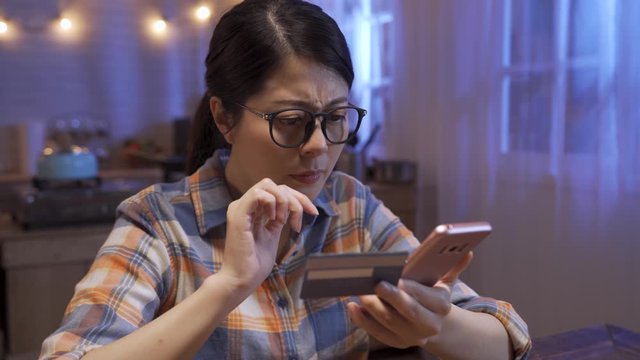 Confused asian korean woman paying online with credit card sitting at home kitchen at night. upset young girl too late buying bargain price on summer sale on internet website in midnight house.