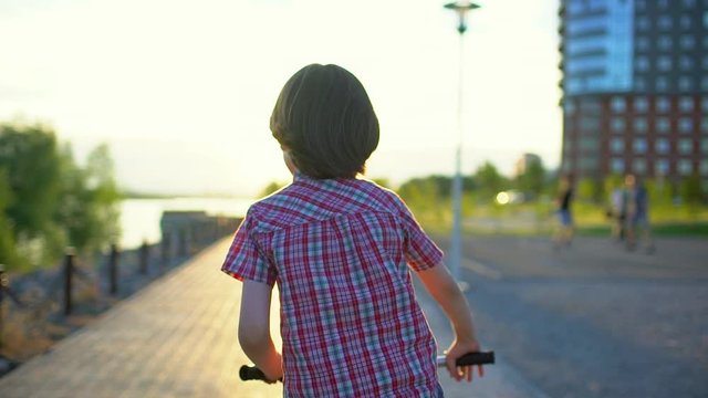 Child little boy riding bicycle on road street at sunset light of summer sunny day. Happy boy kid cycling bike, having fun outdoors nature. Active sport happy family leisure holidays, Slow motion