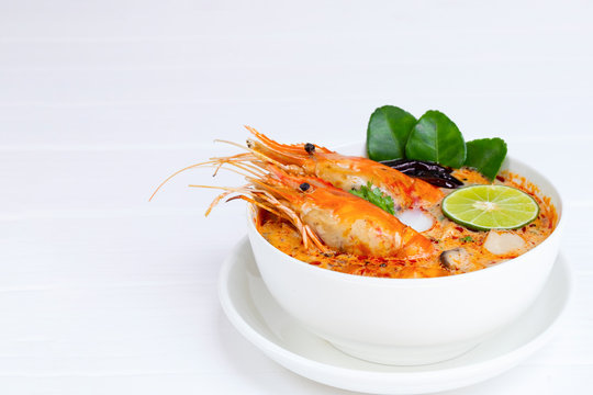 Tom Yum Goong or Shrimp soup spicy sour Soup Traditional food in Thailand contains chili, lime, ginger, galangal, lemongrass, lime leaf, from top view on a white wood background.