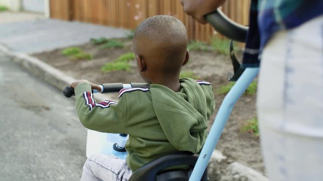 backview of african boy riding push bike tricycle with dad father behind