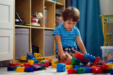 Little Asian child playing with lots of colorful plastic blocks indoor, building high castle.