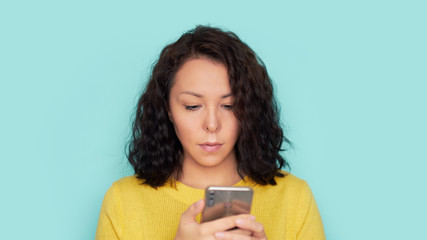 woman using smartphone over blue background. Wearing in in a yellow knitted sweater