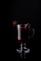 A glass of homemade cranberry-apple mulled wine on a black glossy background. Cinnamon stick. Anise star. Isolate.