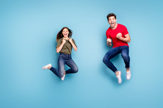 Full body photo of ecstatic two people spouses win lottery jump raise fists scream yeah wear green red t-shirt denim jeans sneakers isolated over blue color background