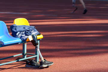 Sneakers, wear and prosthetic leg laying on a seat while their owner run near by