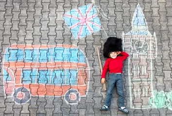 Foto auf Acrylglas Happy little kid boy in british queen's guard soldier uniform having fun with London picture drawing with colorful chalks. With Big Ben, Union Jack and red bus as british doodles. © Irina Schmidt