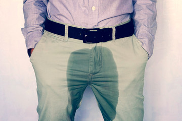 A man standing in wet pants against the wall. Urinary incontinence is an increasingly popular disease affecting younger males. incontinence and wet pants. a dark spot on a light trousers.