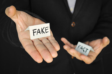 piece of paper with the inscription fake in a man's hand on the background of another hand with the...