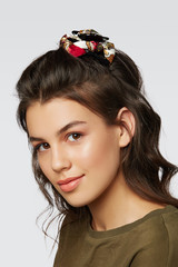 Closeup half-turn face portrait of girl with dark wavy hair, wearing khaki t-shirt. Her hair is pulling with black hairpin crab, decorating with white patterned bow.