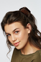 Closeup half-turn face portrait of girl with dark wavy hair, wearing khaki t-shirt. Her hair is...