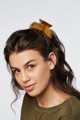 Closeup half-turn face portrait of girl with dark wavy hair, wearing khaki t-shirt. Her hair is...