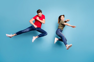 Full size photo of two people crazy funky successful married ninja couple jump practice martial fighting exercises wear green red t-shirt modern outfit isolated over blue color background © deagreez