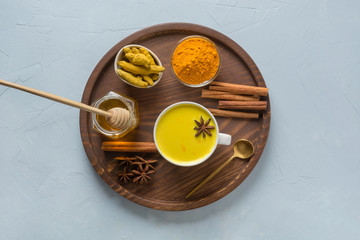Golden turmeric milk with curcuma powder, honey and spices on light blue background. Healthy drink for immunity. Top view.