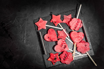Slices of fresh watermelon on dark background. Popsicles in the shape of heart and a star. Top view with copy space