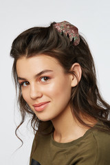 Closeup half-turn face portrait of girl with dark wavy hair, wearing khaki t-shirt. Her hair is...