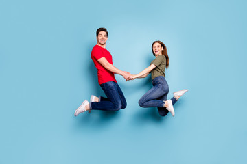 Fototapeta na wymiar Full length profile side photo of charming two person woman man relax rest jump enjoy weekends hold hands wear green t-shirt denim jeans sneakers isolated over blue color background