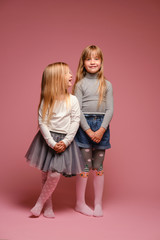 Two little girls are standing on a pink background