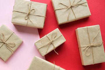 Christmas gifts in gift boxes wrapped in kraft paper and tied with twine lie on a red-pink background. 