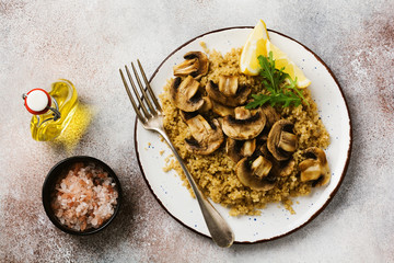 Quinoa, fried mushrooms and lemon for wholesome meal served in simple ceramic plate.  Top view.