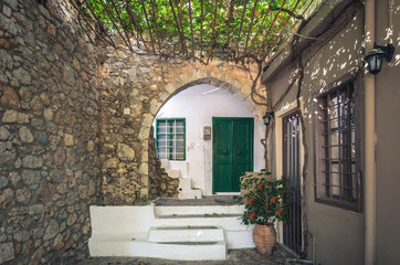 Fototapeta na wymiar Typical greek courtyard with wooden door, stone arch, grapevine and stairs painted in white, in a traditional village of Crete.