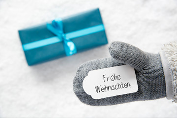 Label With German Calligraphy Frohe Weihnachten Mean Merry Christmas. Gray Glove With Turquoise Gift And Snow Background