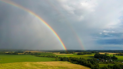 Fototapeta premium Rainbow Above Wheat Field. Flight Down Ripe Crop Field After Rain and Colorfull Rainbow in Background Rural Countryside. Aereal Dron Shoot.