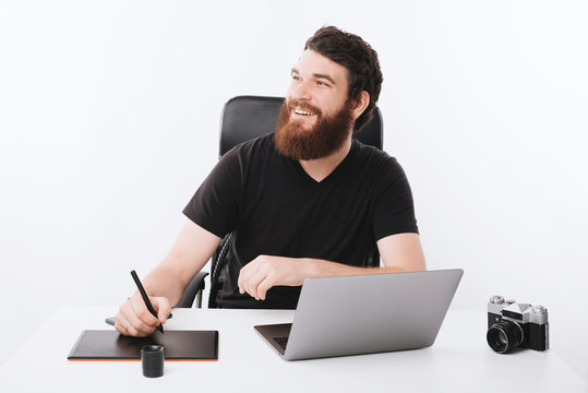 Photo of happy smiling young man working with graphic tablet in office