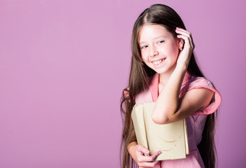 Fiction and nonfiction. Cute small child reading book on violet background. Little girl learn...