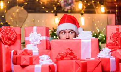 Obraz na płótnie Canvas Holidays filled with fun. Man Santa hat peeking out of pile of gifts. Santa with gifts. Bearded Santa Claus and many holiday packages. Best prices for winter gifts. Seasonal offer. Christmas sale