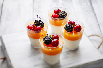 4 cups mango pannacota on wooden tray with blackberries and cherries