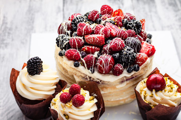 pancake cake with a cap of berries drenched in white chocolate on a wooden white table with a few Belgian muffins