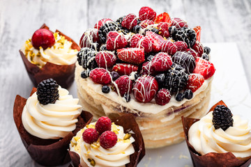 pancake cake with a cap of berries drenched in white chocolate on a wooden white table with a few Belgian muffins