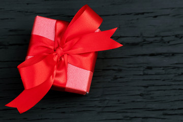 gift box red new year or Christmas Packed present container with red ribbon on Vintage Matte black wooden board background for holiday concept with copy space, top view.