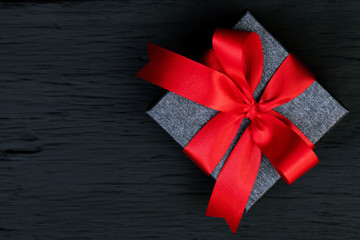 gift box Dark gray new year  Packed present container with red ribbon on Vintage Matte black wooden board background for holiday concept with copy space, top view.