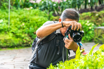 Active Asian Chinese senior male man taking photographs with his digital DSLR camera